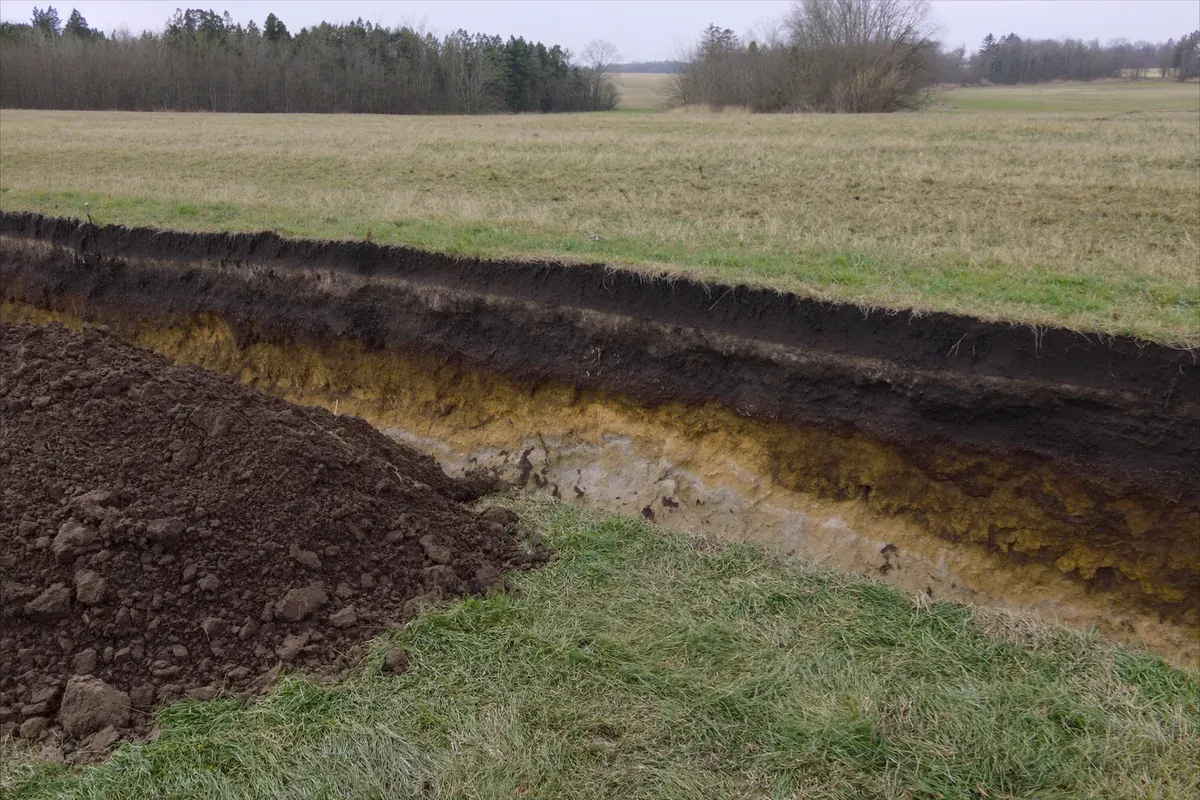 An open soil pit showing dark topsoil over yellow brown subsoil in a Midwest field